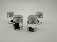Four glass jars filled with clear liquid and black and white glass terp pearls, perfect for dab accessories.