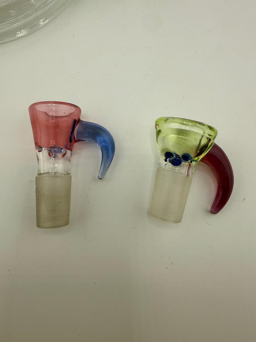 Two handcrafted glass bowls with horn handles, one pink and blue, the other green and red, designed for smoking rigs.