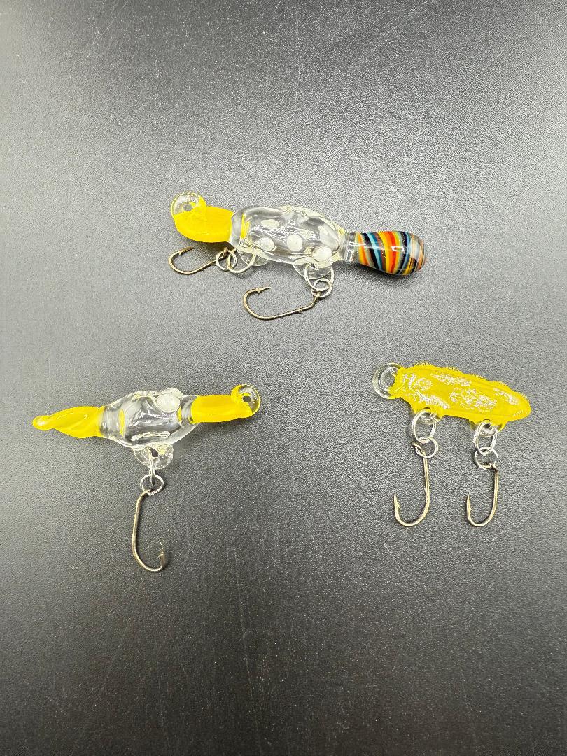 Handcrafted Paulson Pieces glass fishing lures in vibrant colors on a dark surface, showcasing artistry and functionality.