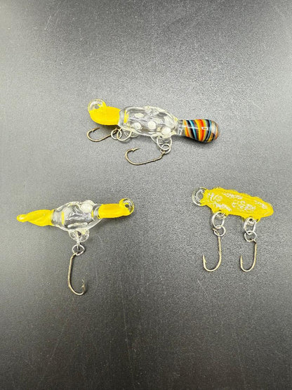 Handcrafted Paulson Pieces glass fishing lures in vibrant colors on a dark surface, showcasing artistry and functionality.