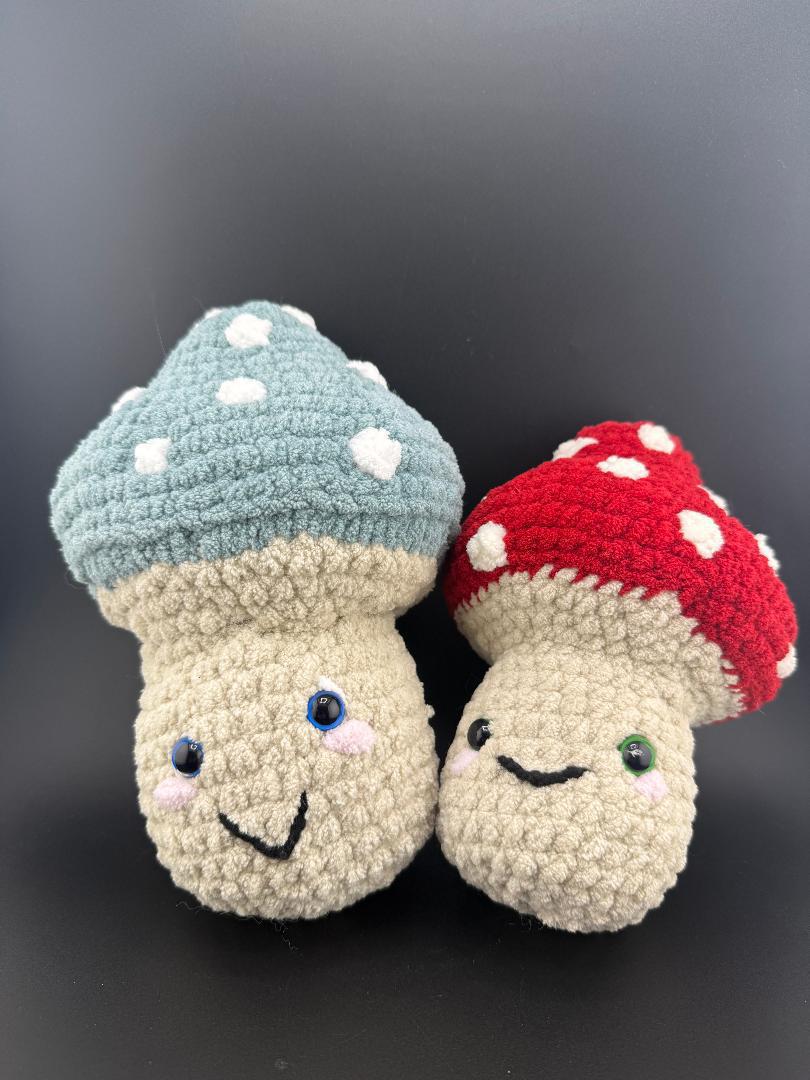 Adorable crochet mushroom plushies in blue and red, featuring cute smiles and polka dots, perfect for decor or gifts.