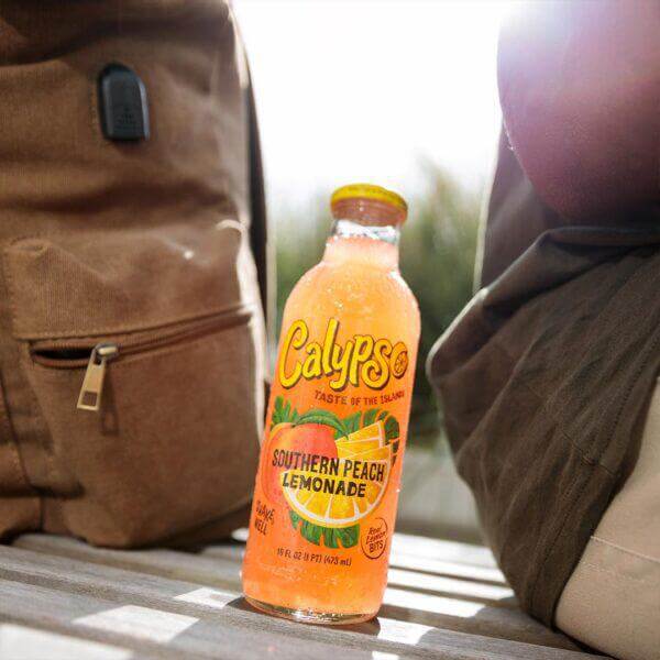 Calypso Southern Peach Lemonade 16oz bottle featuring vibrant packaging, surrounded by outdoor elements.