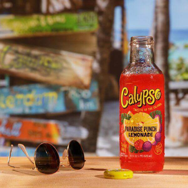 Calypso Paradise Punch Lemonade 16oz bottle beside sunglasses on a tropical background