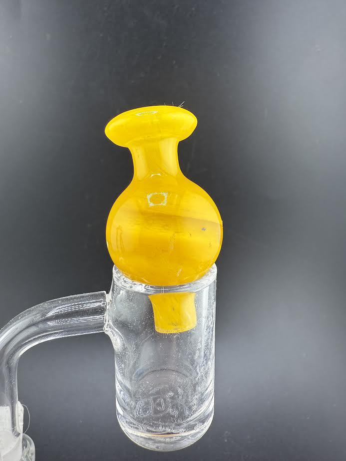 Bright yellow Bolt Up Bubble Cap resting on a glass banger, enhancing vapor control and airflow.