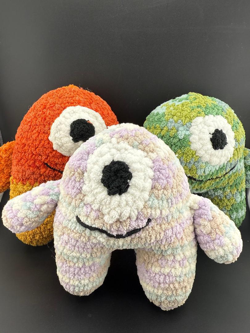 Colorful crochet one-eyed monsters in plush form, perfect for cuddling and play.