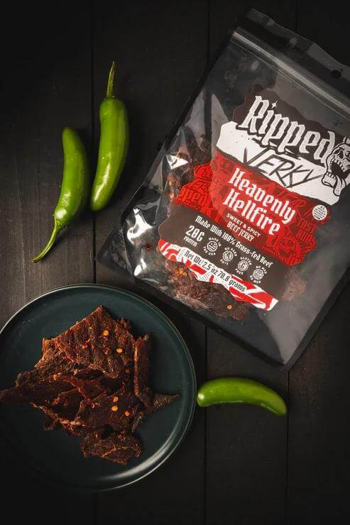 Ripped Jerky Heavenly Hellfire bag with spicy jerky and green peppers on a black table.