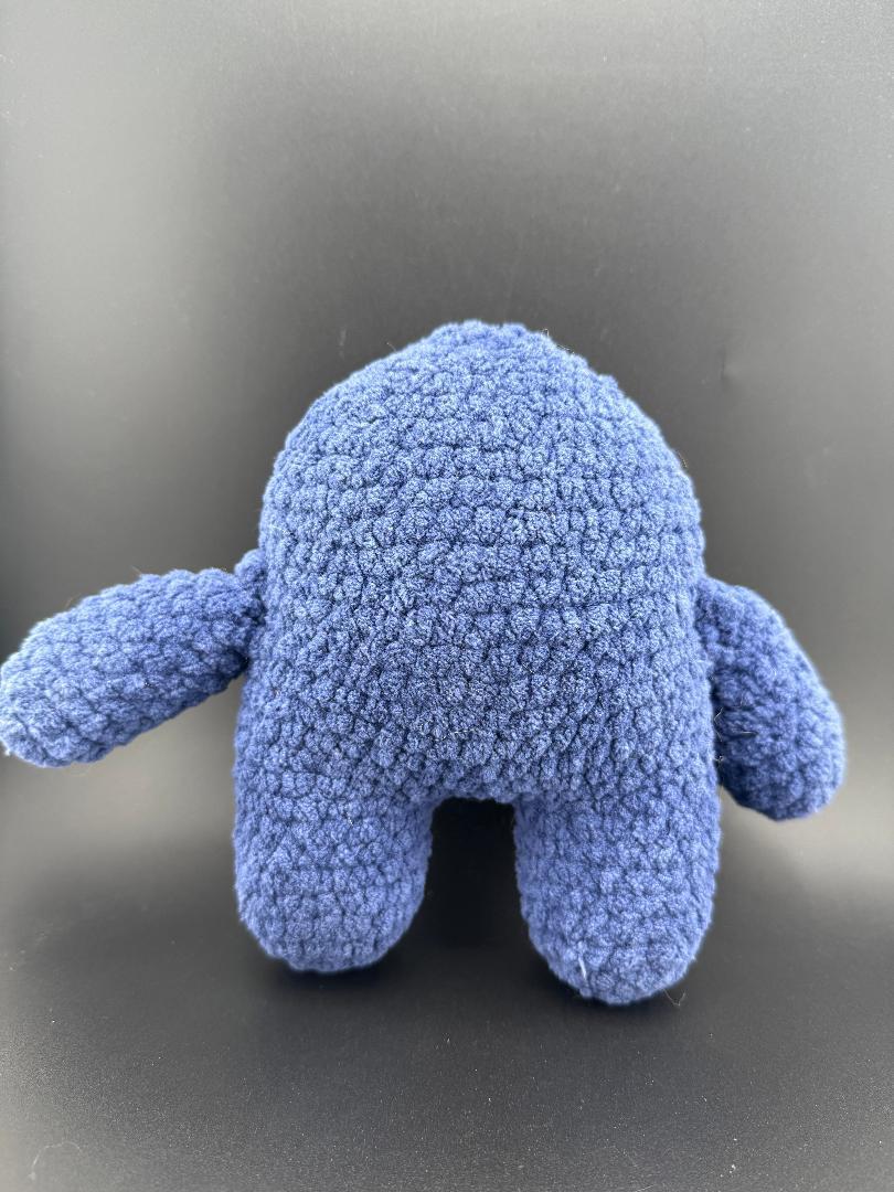 Back view of a cute blue crocheted one-eyed monster plush toy with arms.