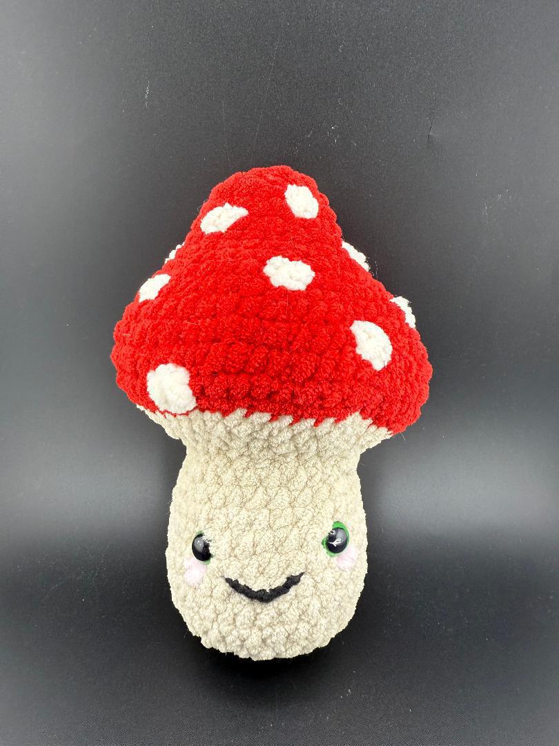 Adorable crochet mushroom plushy with red cap and white spots, featuring a smiling face, perfect for cuddling.