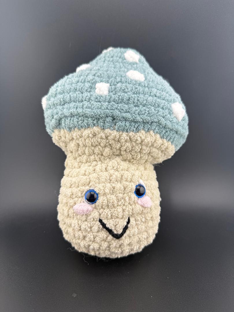 Crochet mushroom plushy with a smile, blue cap and white spots, perfect for kids and collectors.