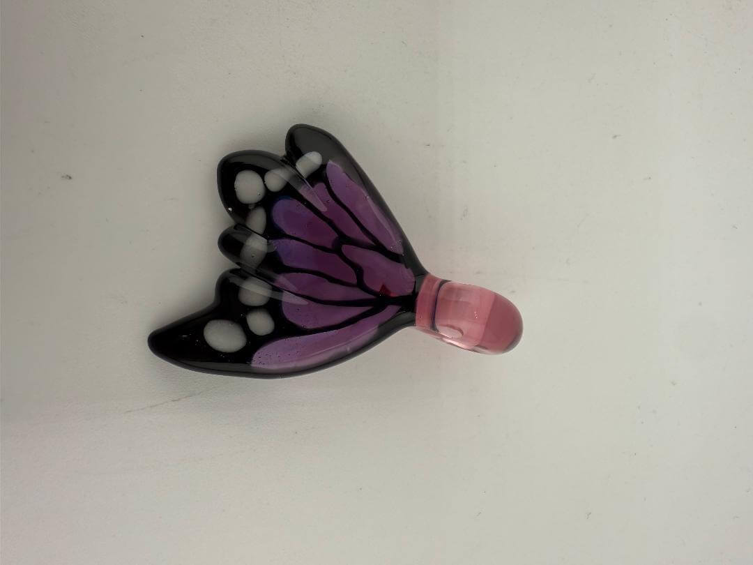 Colorful glass pendant designed as a butterfly wing, featuring purple and pink details, on a plain background.