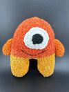 Crochet one-eyed monster plush toy in orange and yellow hues, perfect for kids and quirky decor.
