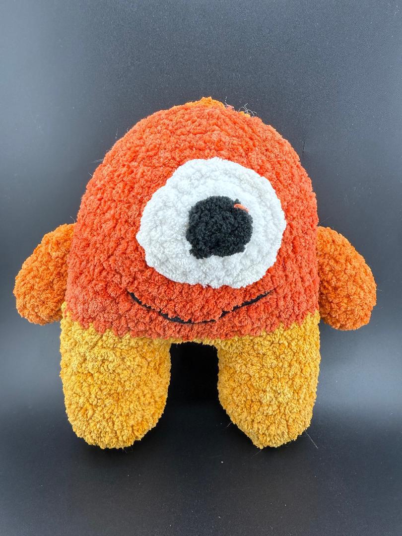 Crochet one-eyed monster plush toy in orange and yellow hues, perfect for kids and quirky decor.