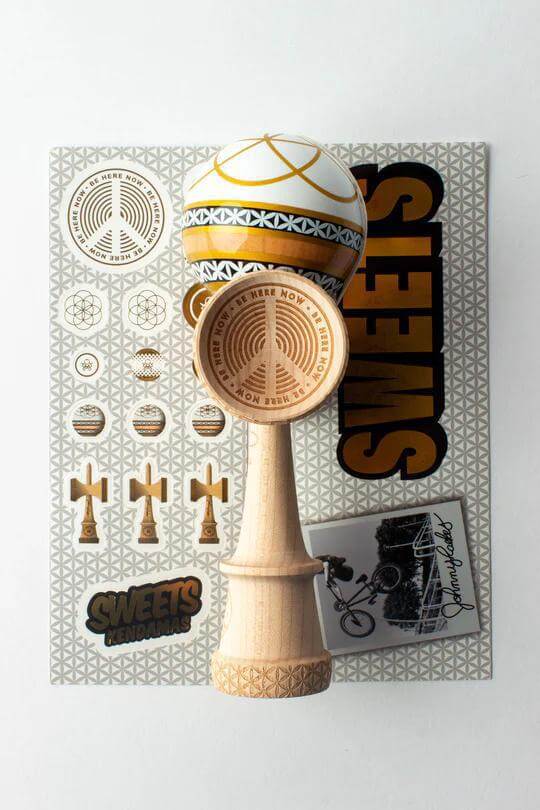 Sweets Kendama Johnny Raekes Amped model, featuring design elements and stickers on a textured background.