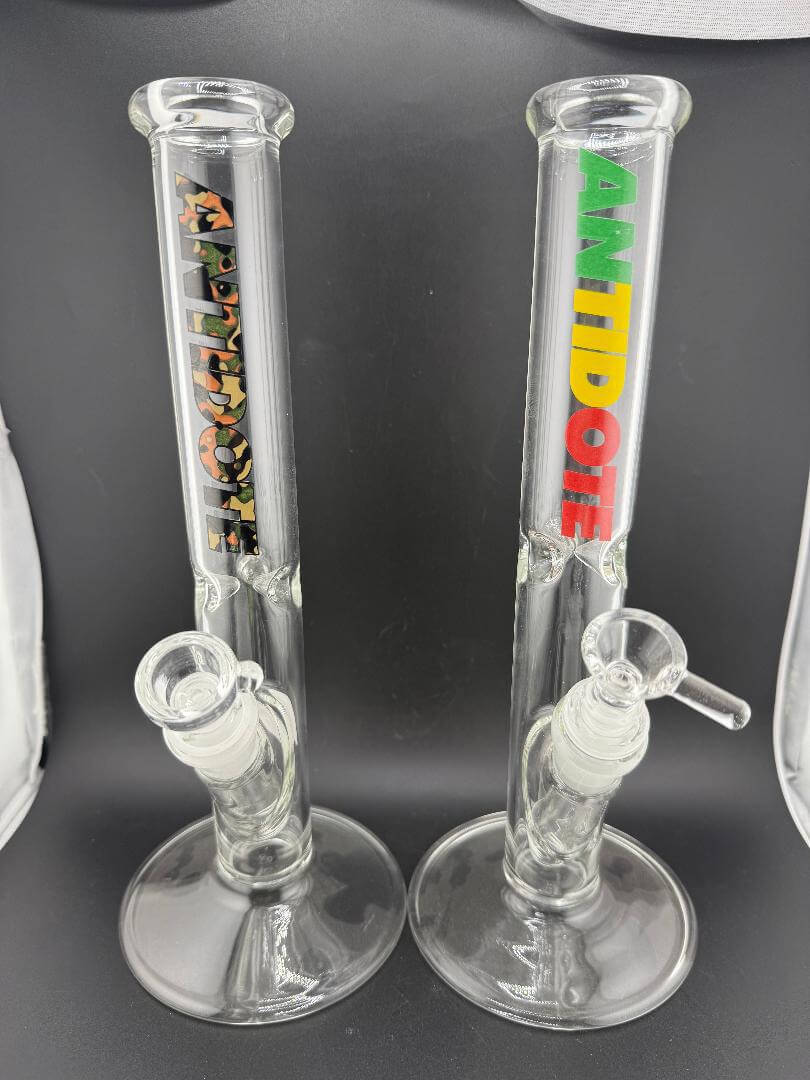 Antidote Glass Slim Straight Tube 14mm 45° in camo and rasta logo designs, showcasing premium borosilicate glass.