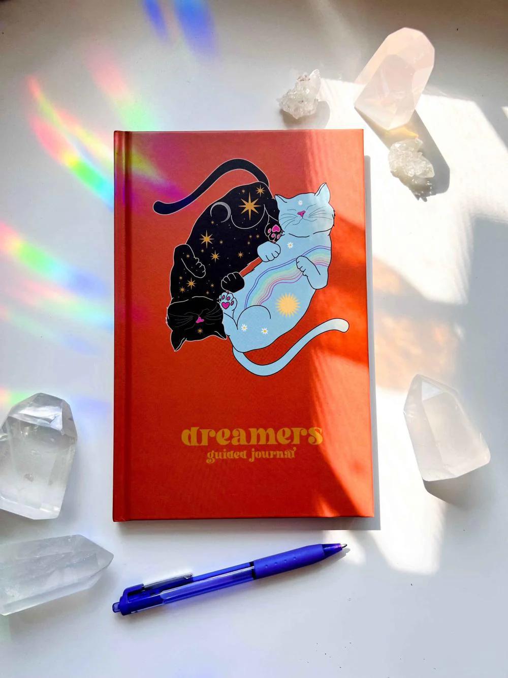 Ark Made Dreamers Guided Journal on a table with crystals and a pen, featuring colorful cat illustrations and a vibrant cover.