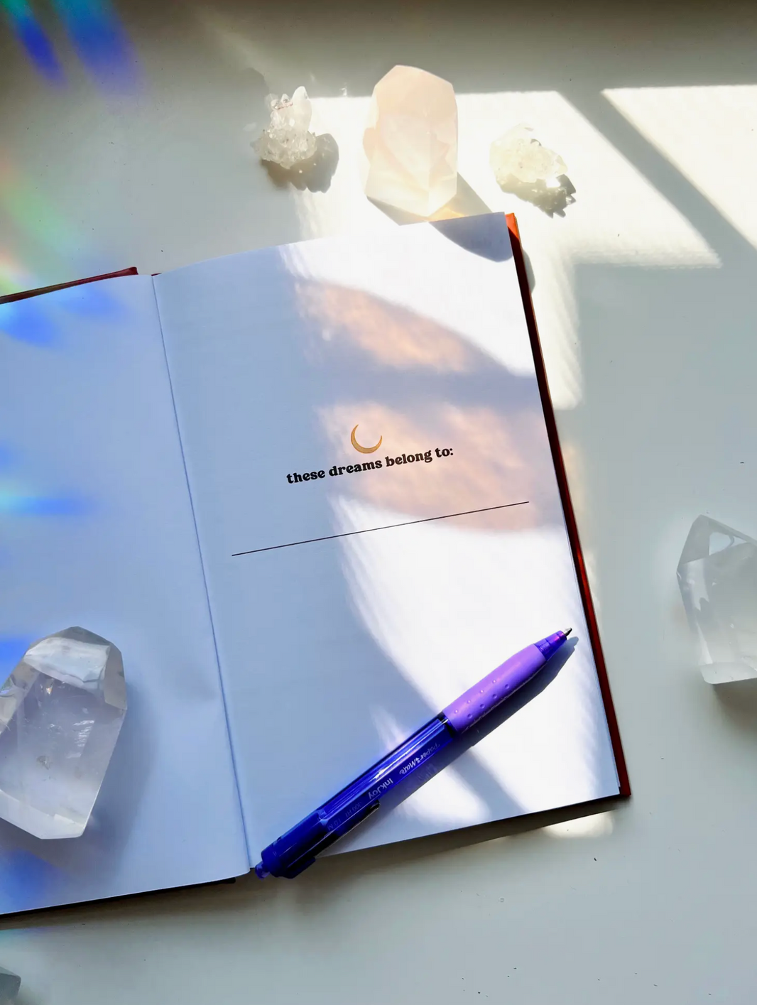 Ark Made Dreamers Guided Journal open page with text 'these dreams belong to' and a pen, surrounded by crystals.