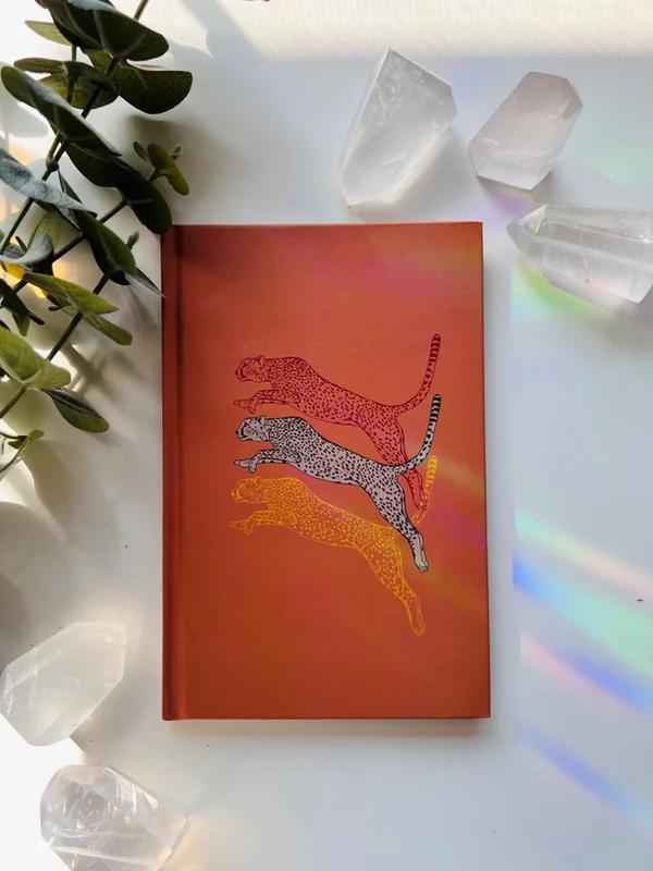 Ark Made Leaping Leopards Lined Journal with colorful leopard illustrations on an orange cover, surrounded by crystals.