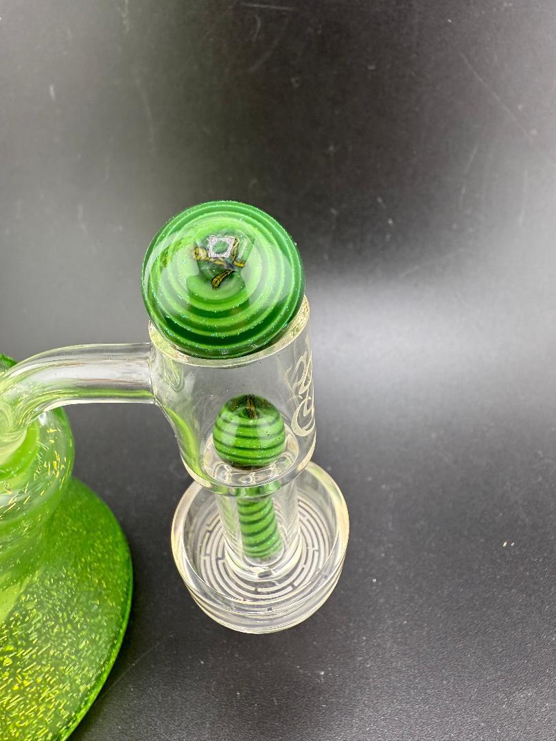 Close-up of a green glass bong with striped millie design bowl and dab function features.
