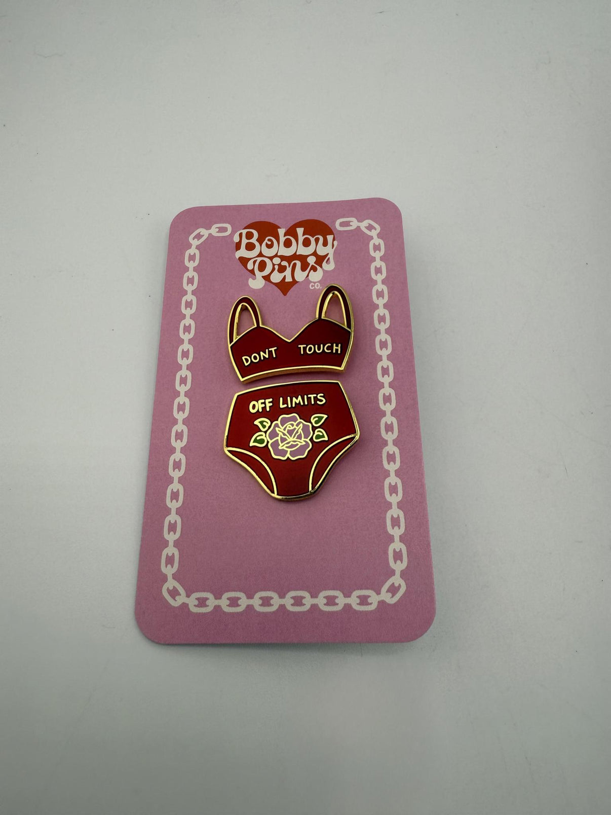 Bobby Pins Co. Enamel Pin - Lingerie Red featuring a playful lingerie design on a pink backing.