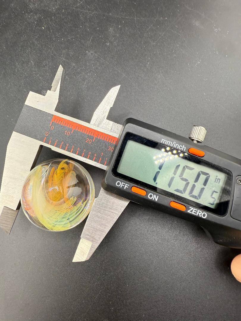 Brando Glass Marble - Fumed Implosion being measured at 1.150 inches showcasing its vibrant color and craftsmanship.