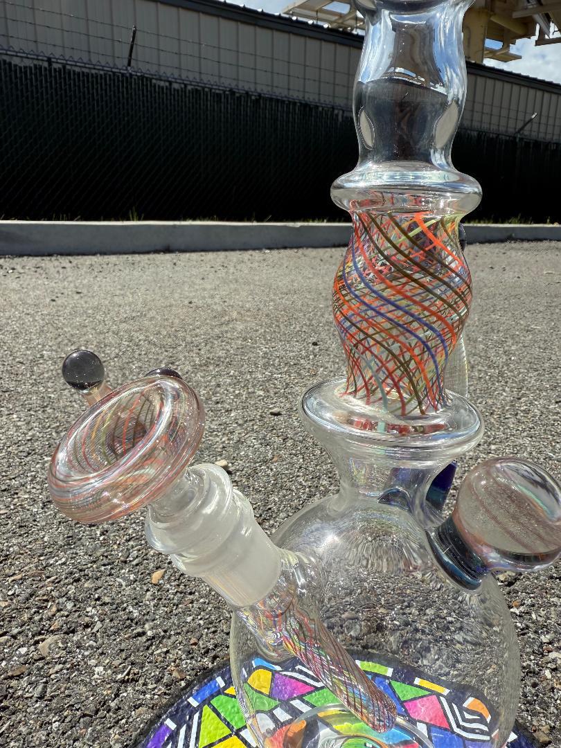 Close-up of Brando Glass Retti Rainbow Tube showcasing vibrant reticello pattern and craftsmanship on an outdoor surface.