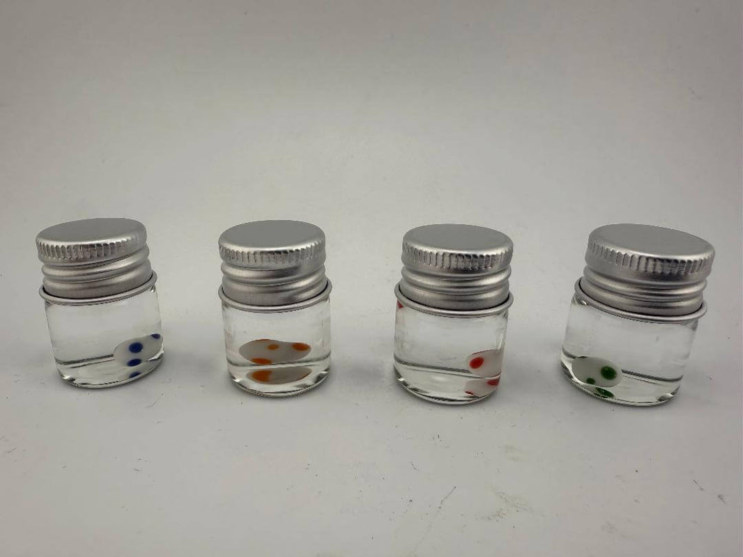 Four glass jars with colorful terp pearls inside, showcasing blue, orange, red, and green options for dab enthusiasts.