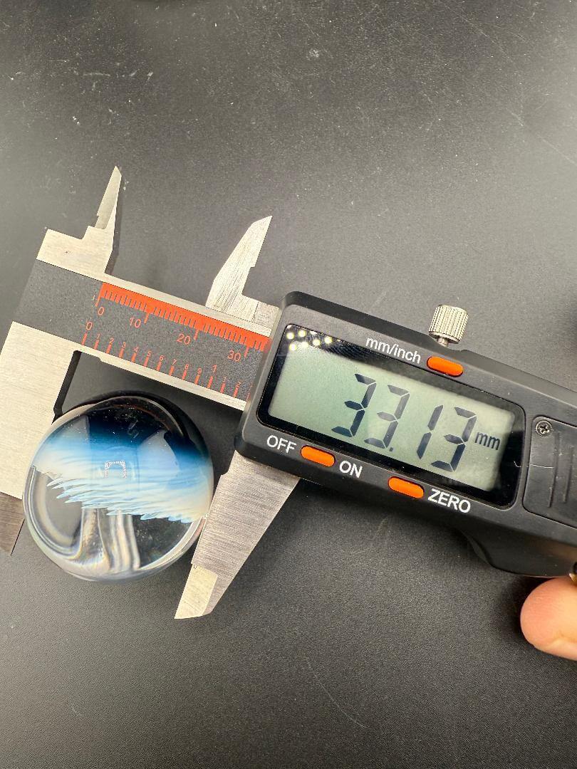 Danny W Glass Marble - 33mm White Implosion measuring 33.13mm with calipers on a black background.