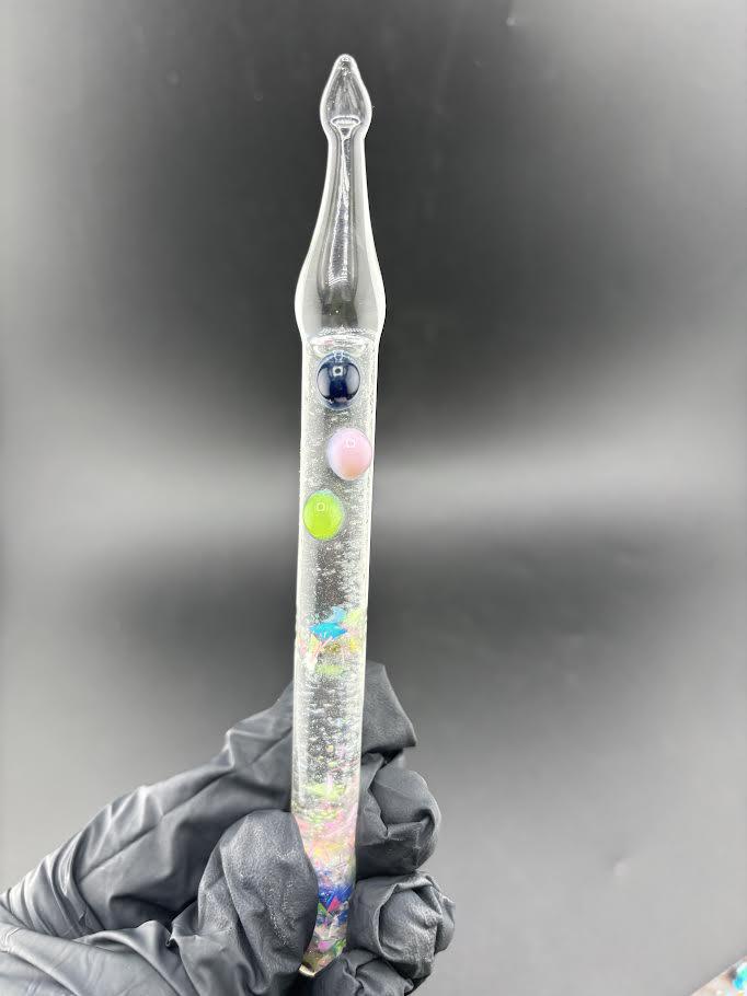 Dollhouse Glass Glitter Dab Tool with floating glitter designs in a clear handle, held with a gloved hand.