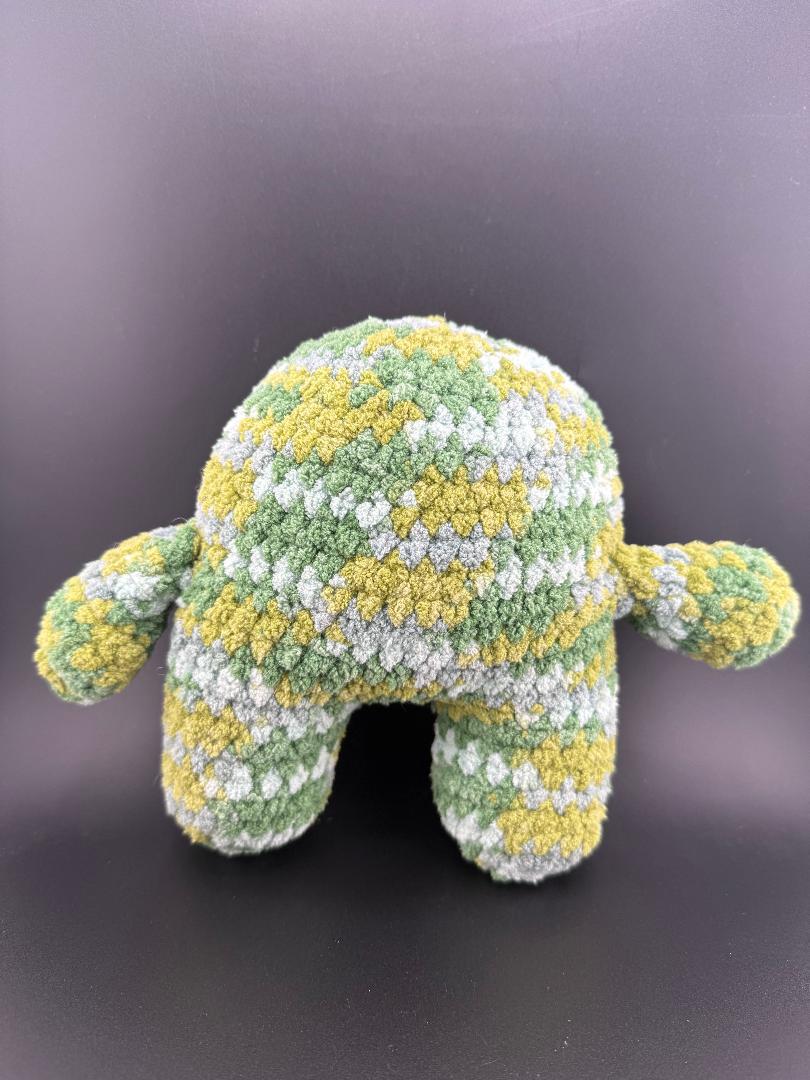 Crochet one-eyed monster plush in green and yellow textured yarn, perfect for cuddling or as a unique decor piece.