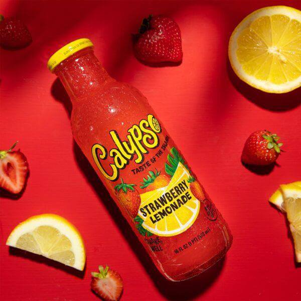 Calypso Strawberry Lemonade 16oz bottle surrounded by fresh strawberries and lemon slices on a vibrant red background.