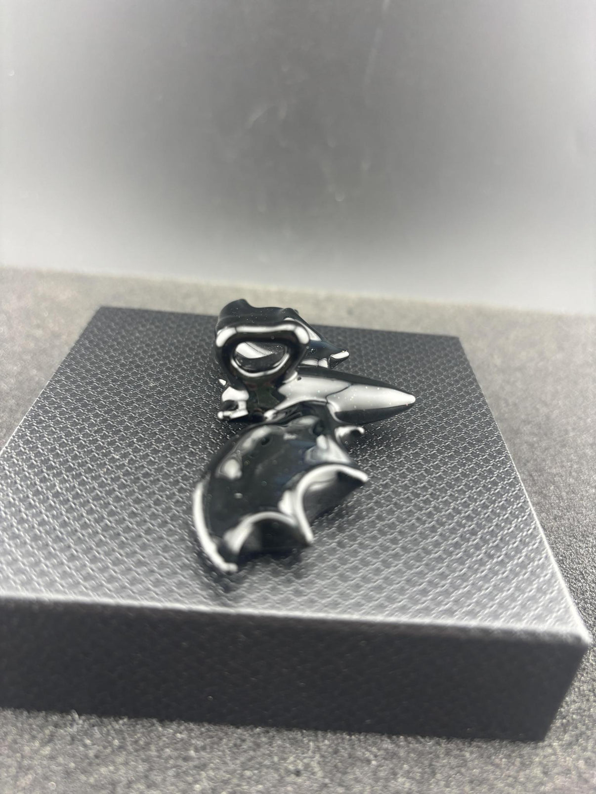 Filla John Bat Pendant displayed on a textured box, showcasing its unique black handcrafted design.