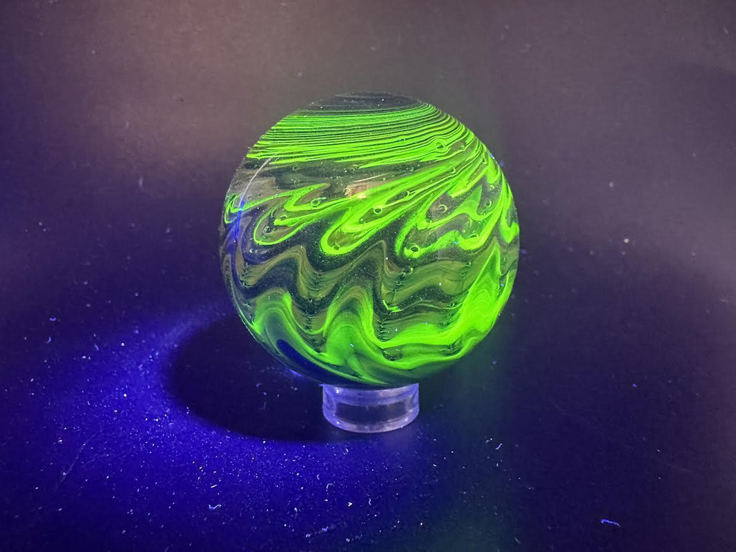 Filla John Glass Big Marble - Sparkled Swirls UV resting on a display stand with vibrant green swirling patterns.