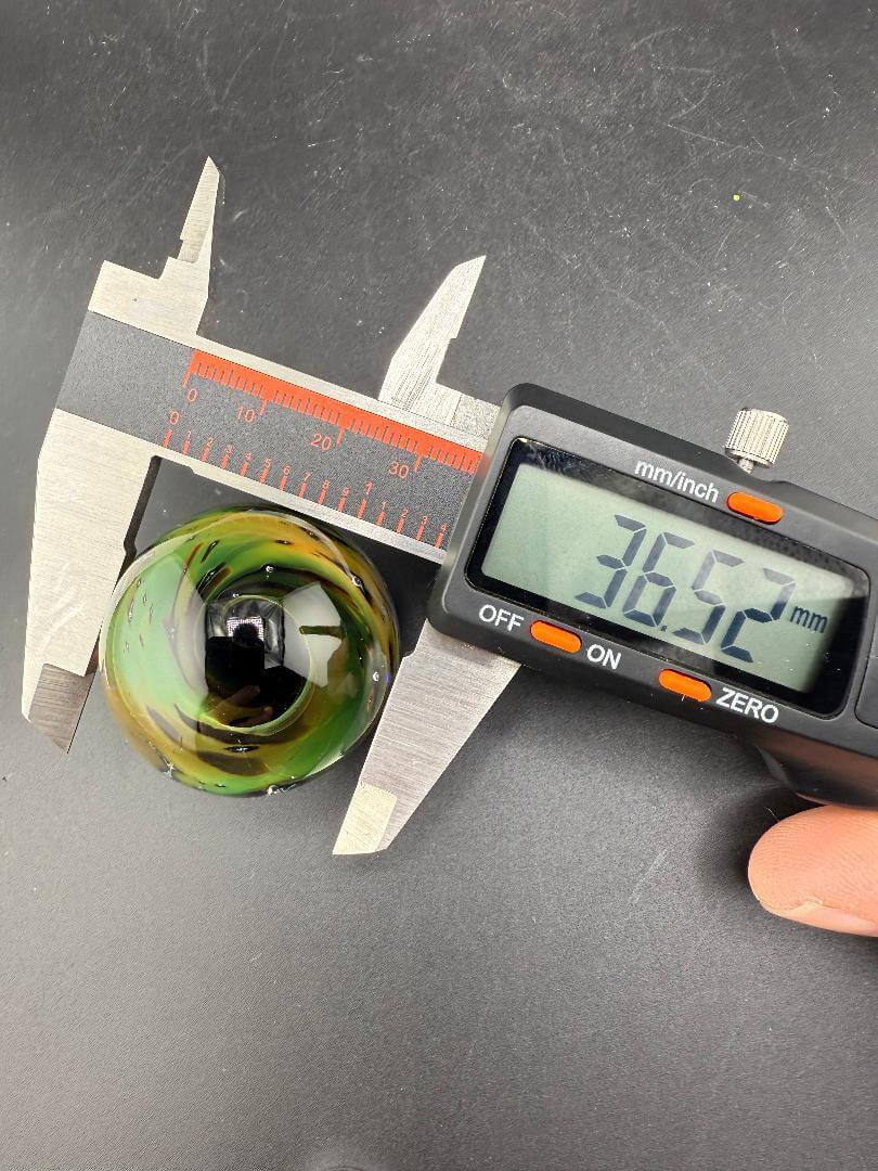 Filla John Glass Marble - 36mm Green Space Tech shown with calipers measuring its diameter at 36.5mm.