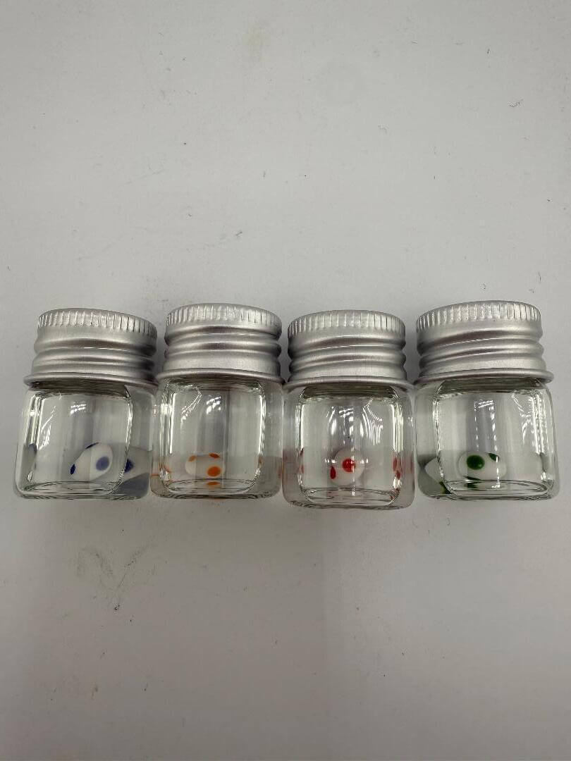 Set of four small glass jars with metal lids, each featuring a colorful dot design inside.