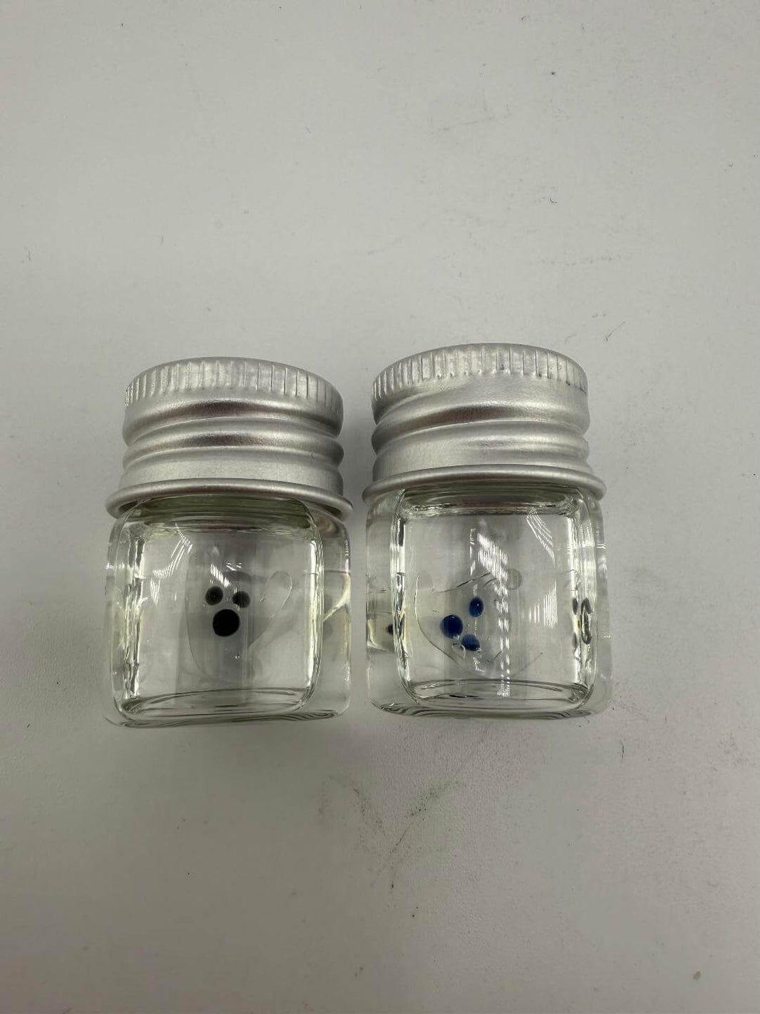 Two small glass jars with silver lids, featuring colorful dots inside for storage or decoration.