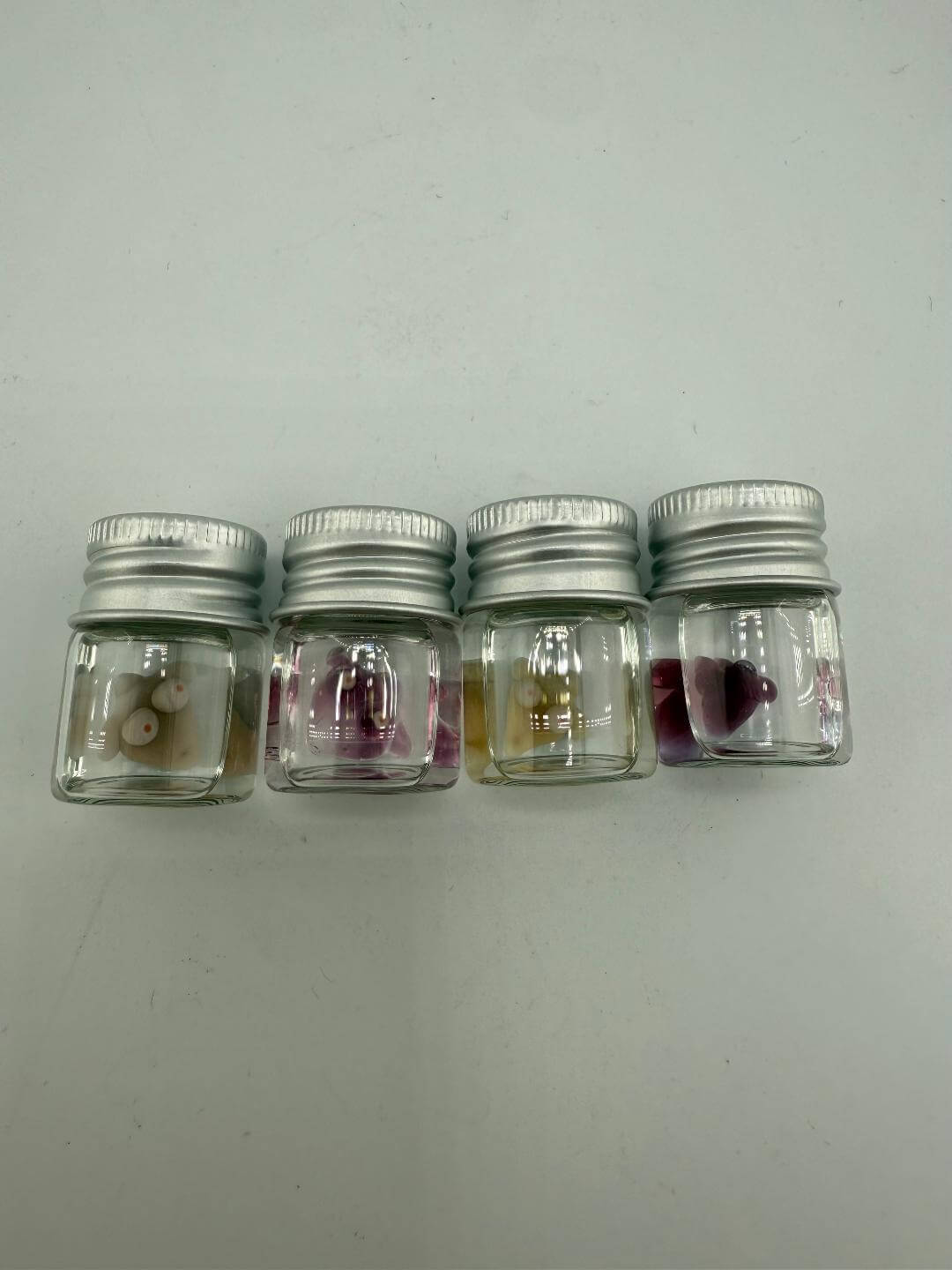 Four small glass jars containing colorful terp pearls, showcasing unique designs for dabbing accessories.