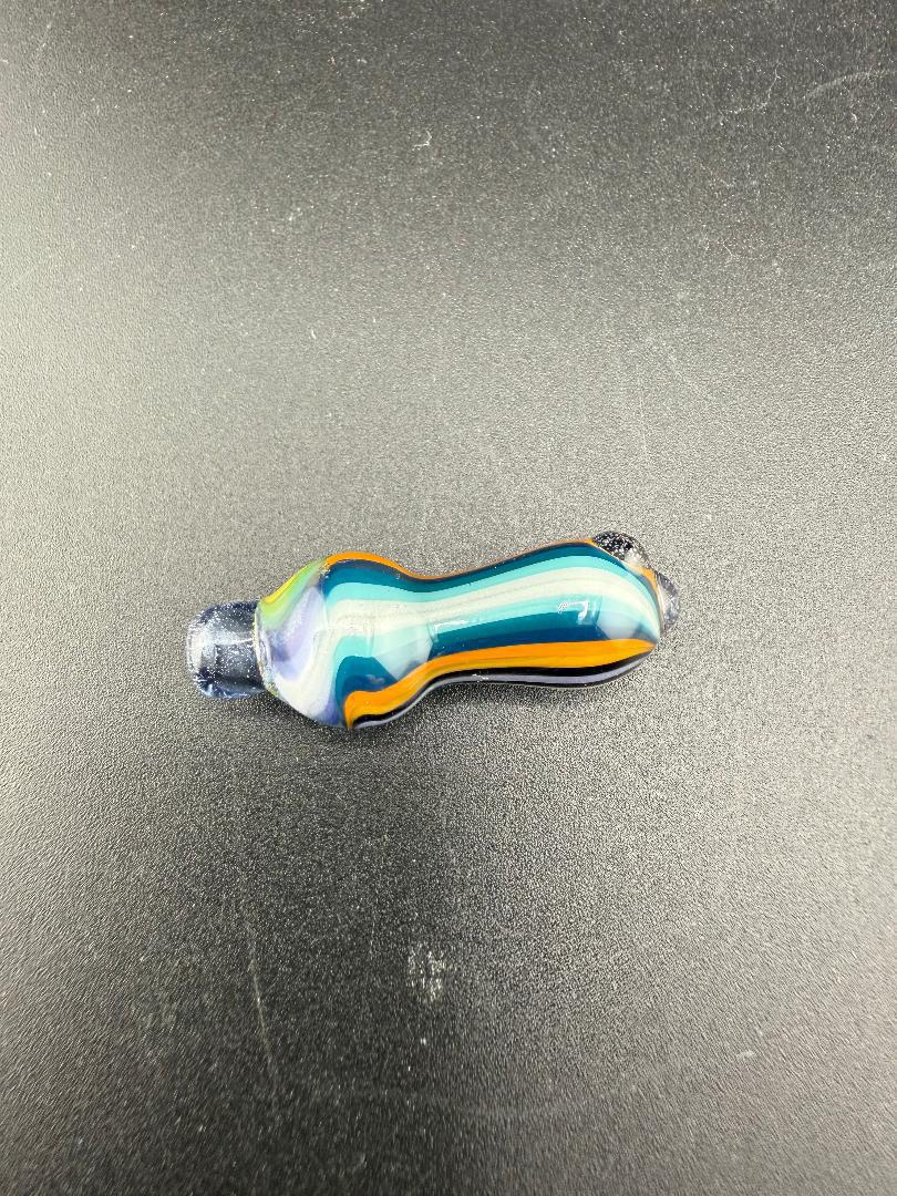 Colorful handcrafted glass piece with blue, orange, and purple swirls resting on a black surface.