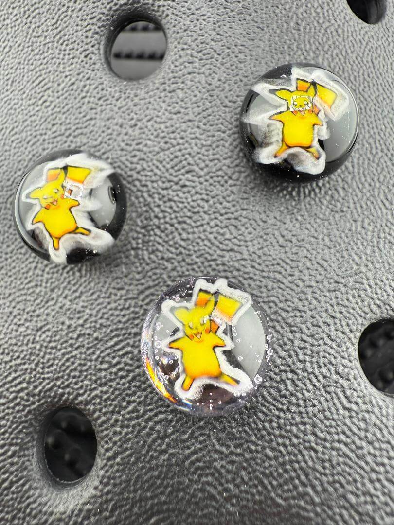 Three handcrafted glass giblets featuring a yellow pop culture character on a textured black background.