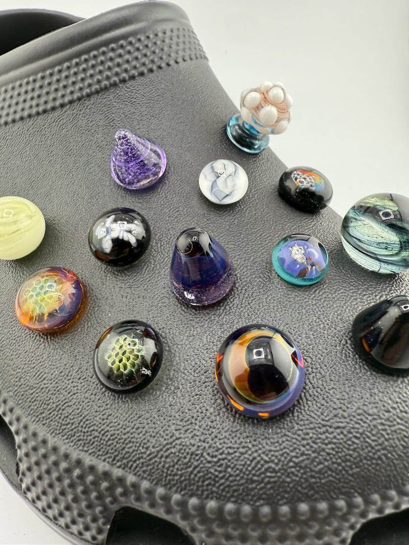 Colorful handcrafted glass giblets displayed on a black Crocs shoe, showcasing pop culture-inspired designs.