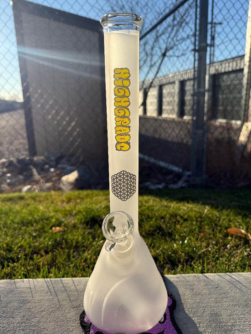 Highgrade Glass Flower Beaker - Sandblasted w/ Sacred Geometry Bake on 14mm 45° standing on grass, showcasing its design and craftsmanship.