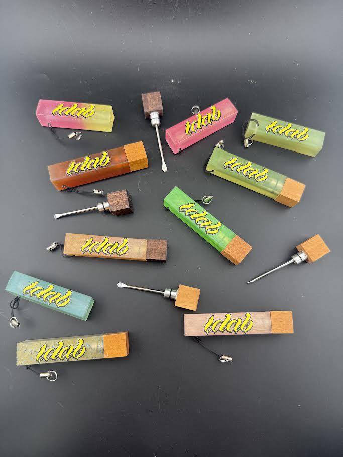 Collection of colorful Idab Dabber Guard tools for concentrate sessions laid out on a black background.