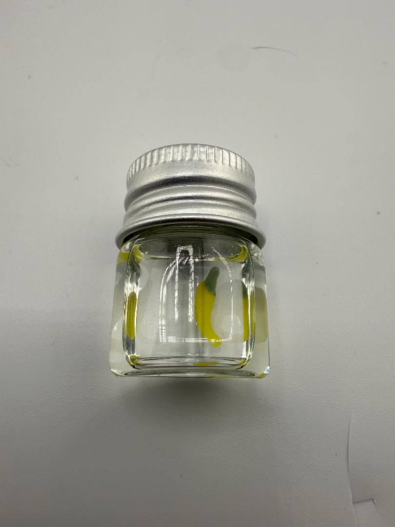 Clear glass jar with a silver lid, containing yellow banana-shaped terp pearl for dabbing accessories.