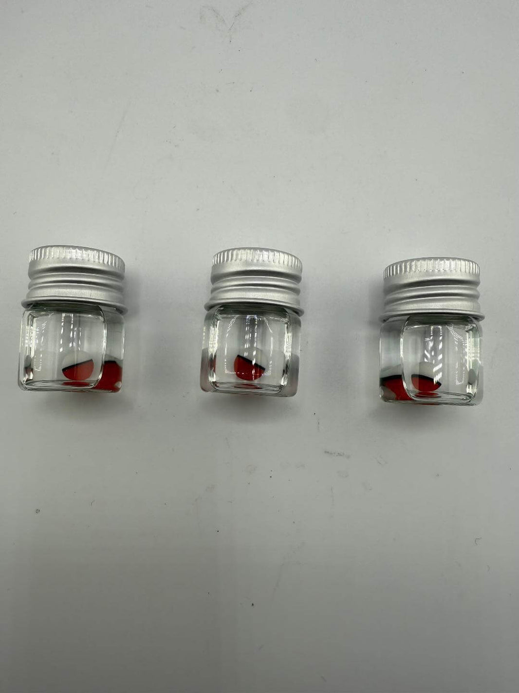 Three small jars containing red glass pieces, ideal for crafting or storage, on a white background.