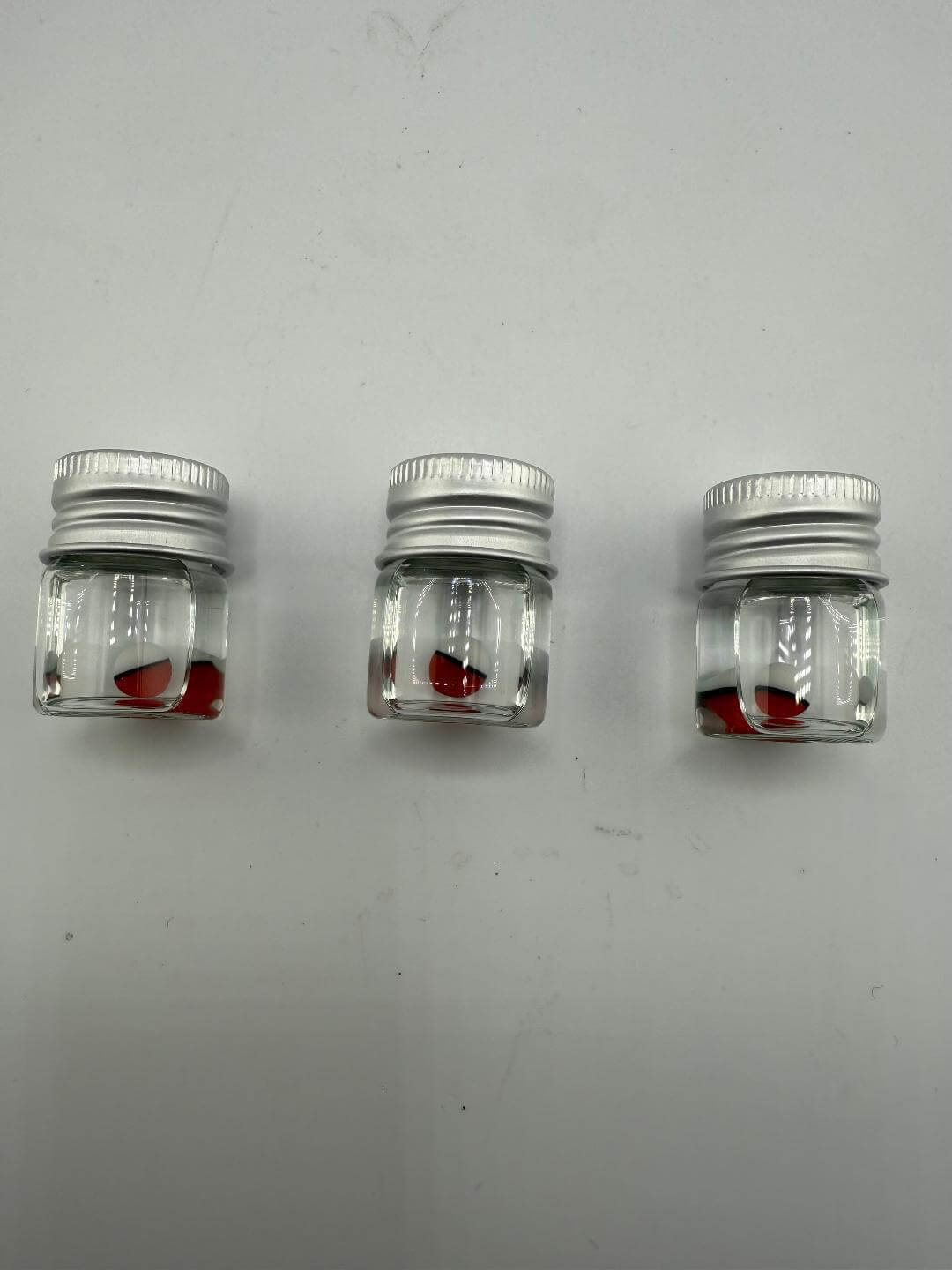 Three small jars containing red glass pieces, ideal for crafting or storage, on a white background.