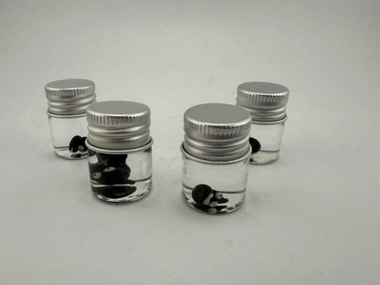 Four glass jars filled with clear liquid and black and white glass terp pearls, perfect for dab accessories.