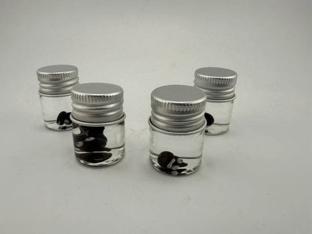 Four glass jars filled with clear liquid and black and white glass terp pearls, perfect for dab accessories.