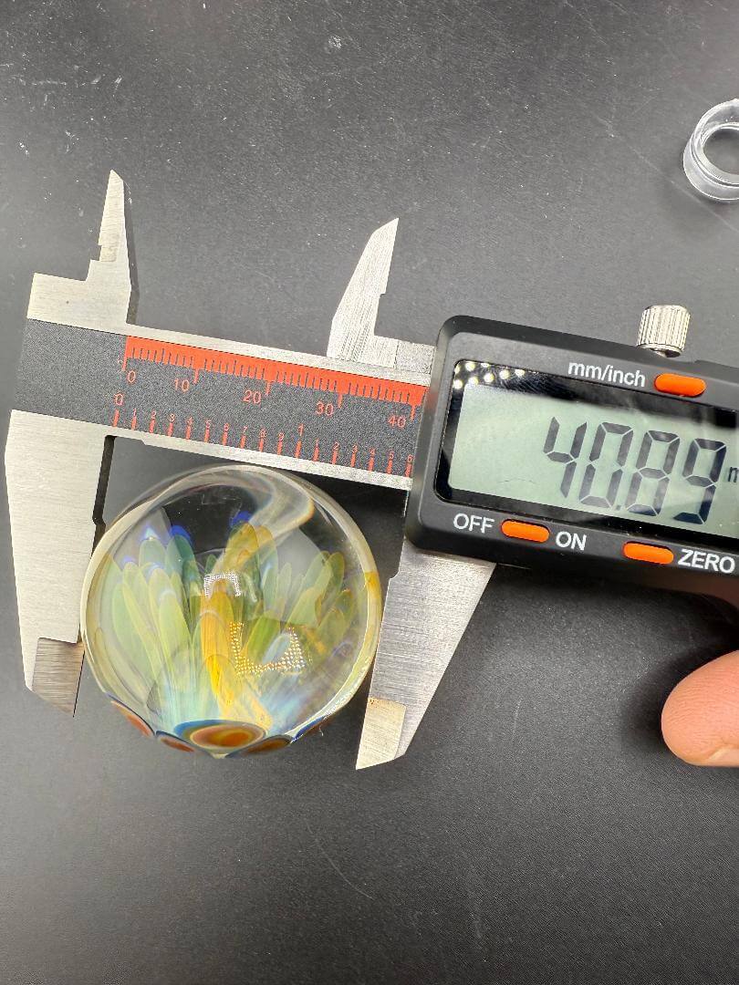 McDoogIe Glass Marble – 40mm Gold Fume Implosion being measured with calipers, showing vibrant colors and depth.