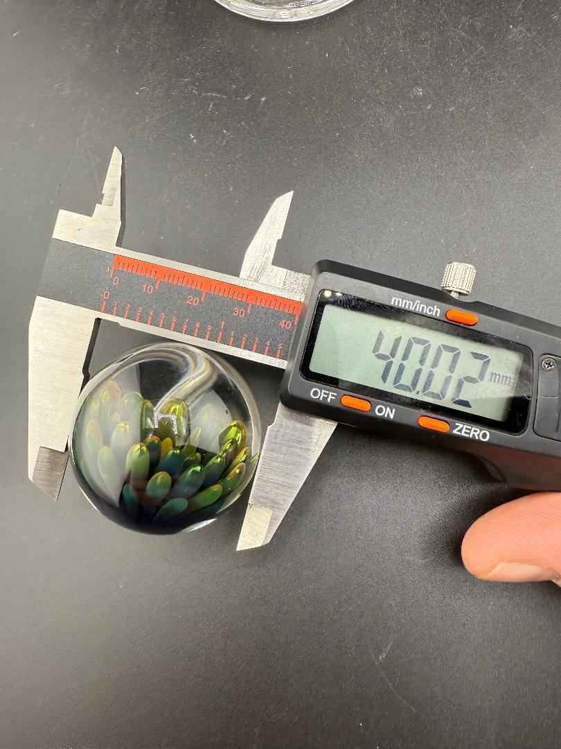 McDoogIe Glass Marble – 40mm Gold Fume Implosion measured at 40.02mm with calipers on a black surface.
