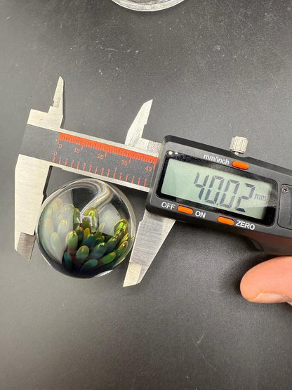 McDoogIe Glass Marble – 40mm Gold Fume Implosion measured at 40.02mm with calipers on a black surface.