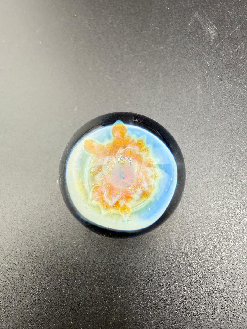 Mcdoogle Glass Marble - 22mm No Fume Fume Tech w/ Purple Flower Dot Stack Backer on a dark surface.